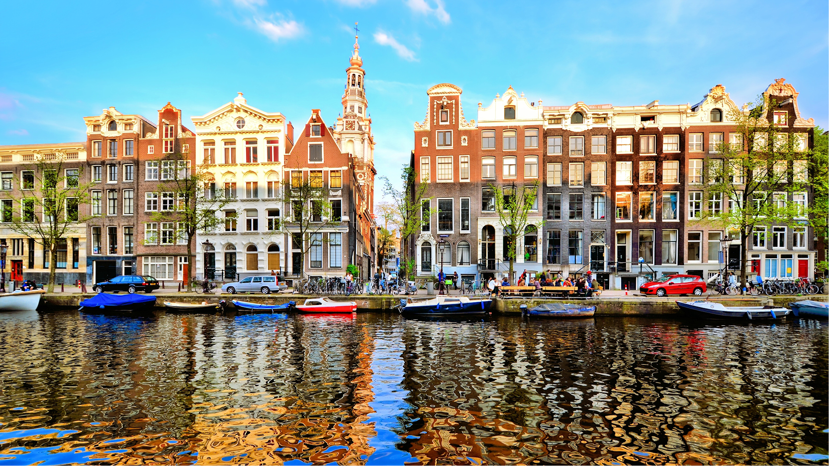 Spegelblanka kanaler med båtar och husfasader i alla dess färger i Amsterdam.